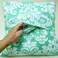 a hand is holding the edge of a green and white pillow