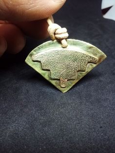 a hand holding a small green pendant with an intricate design on it's side