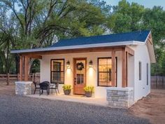 a small white house sitting on top of a gravel lot next to trees and bushes