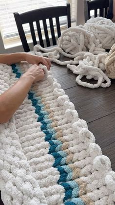 two people are crocheting together on a table with chairs and a rug in the background