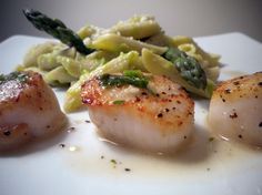 three scallops on a plate with pasta and asparagus garnish