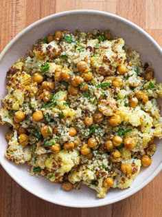 a white bowl filled with cauliflower and chickpeas covered in rice on top of a wooden table