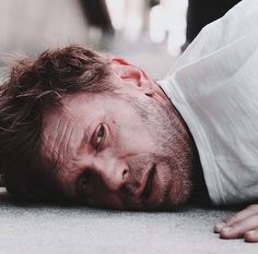 a man laying on the ground with his head in his hands and looking at the camera