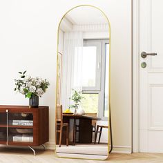 a mirror sitting on top of a wooden floor next to a table with flowers in it