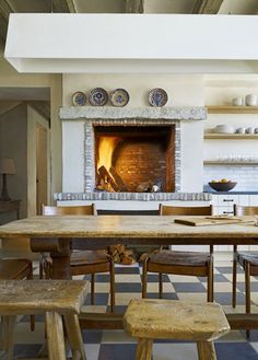 a dining room table with chairs and a fire place in the fireplace behind it on a checkered tile floor