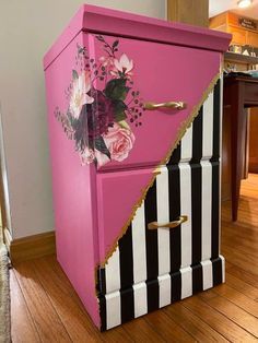 a pink and black striped chest with flowers painted on the side, sitting on a hard wood floor