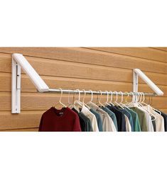 a rack with clothes hanging on it next to a wooden wall and a white coat hanger