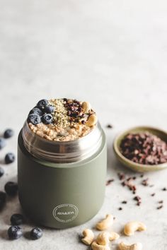 a green jar filled with oatmeal and blueberries next to some nuts