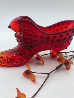 a red glass bird sitting on top of a branch next to some leaves and flowers