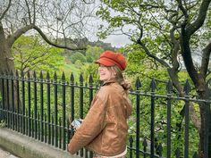 a woman standing next to a fence looking at her cell phone and wearing a red hat