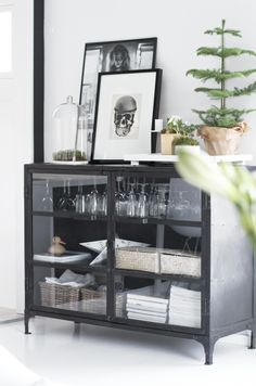 a black cabinet filled with wine glasses next to a potted plant and framed pictures