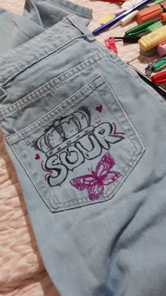 a pair of blue jean pants sitting on top of a bed next to crayons