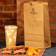 a sandwich and drink sitting on a table next to a brown paper bag