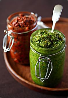 two jars filled with green food on top of a wooden tray