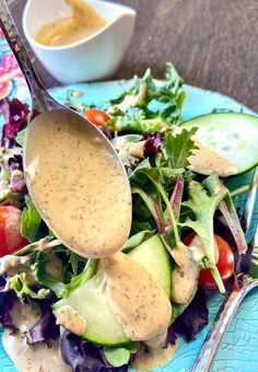 a salad with dressing being spooned into it on a blue plate next to a white bowl