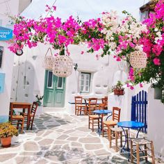 an alleyway with tables and chairs lined up against the wall, flowers hanging over them