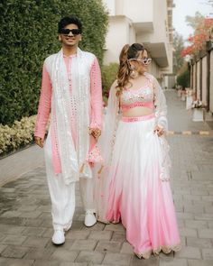 two people dressed in white and pink are walking down the street with sunglasses on their heads