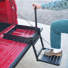 a man is sitting on the back of a red truck and pulling something with his feet