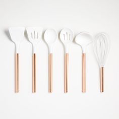 five utensils lined up next to each other on a white surface with copper tips