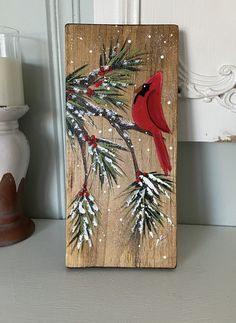 a red cardinal sitting on top of a pine tree next to a white candle holder