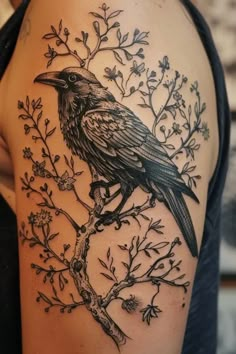 a black bird sitting on top of a tree branch with leaves and branches around it