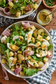 two white bowls filled with salad on top of a wooden table next to utensils