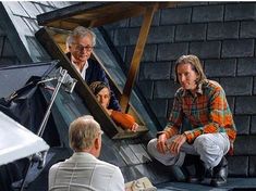 an older man sitting on the ground next to two women and a man standing in front of him