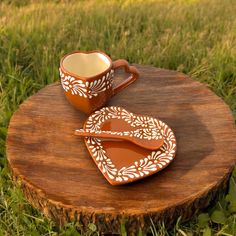 two coffee mugs sitting on top of a tree stump in the grass, one is shaped like a heart