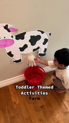 a young boy is playing with a cow cut out on the wall behind him that says toddler themed activities farm