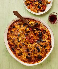 two bowls of food on a table with wine and glasses next to it, one bowl has an eggplant casserole