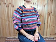 a woman sitting on top of a wooden bench wearing a colorful sweater and bracelets