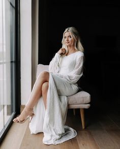 a woman is sitting on a chair in front of a window and posing for the camera