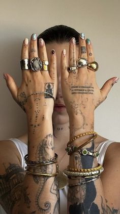 a woman with tattoos covering her eyes and hands behind her head is covered by various bracelets