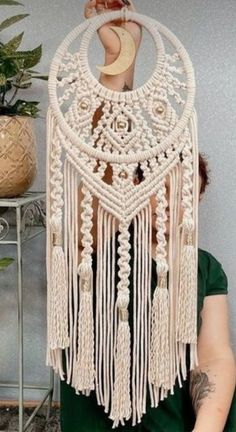 a woman wearing a green dress and holding up a white macrame dream catcher