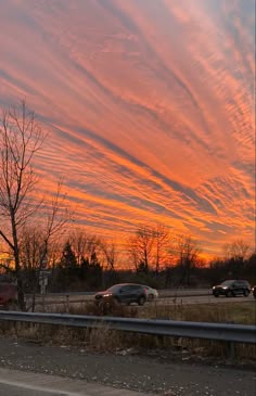 the sky is pink and orange as cars drive down the road in front of them