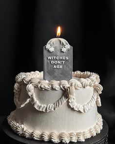 a white cake with a lit candle on top that says witches don't age