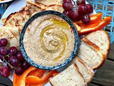 a bowl of hummus surrounded by sliced bread and grapes