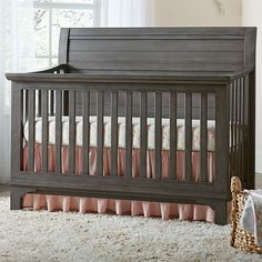 a baby crib with pink and white bedding next to a basket on the floor