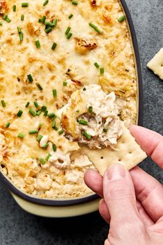 a hand holding a tortilla chip with chicken and cheese in it next to crackers