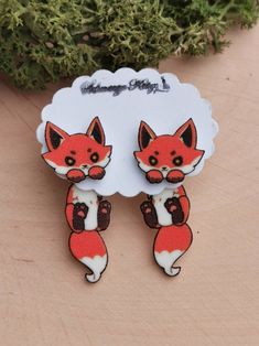 a pair of fox earrings sitting on top of a wooden table