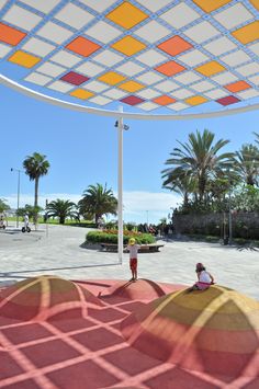 a person standing under a colorful umbrella on top of a sandy beach next to palm trees