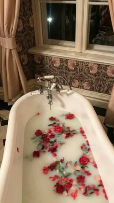 a bathtub filled with water and red roses floating in it next to a window