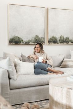 a woman sitting on top of a white couch next to two pictures above her head