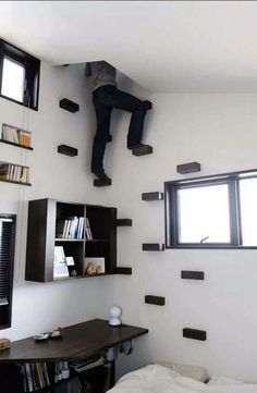 a man is hanging upside down from the ceiling above a bed in a room with bookshelves