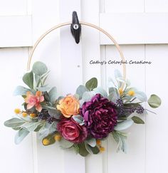 a wreath with flowers hanging on the side of a white door that says catty's colorful creations