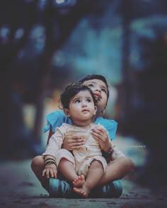 two children sitting on the ground with their arms around each other and looking up at something