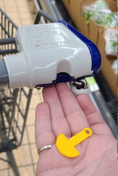 a hand holding a yellow and blue object in it's right hand next to a shopping cart