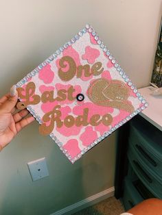 someone holding up a pink and gold graduation cap with the words one last rodeo on it