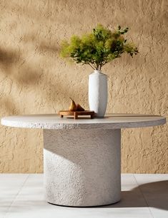 a white vase sitting on top of a table next to a potted green plant