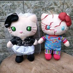 two hello kitty dolls sitting next to each other on top of a wooden table in front of a stone wall